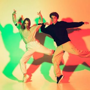 Young beautiful man and woman dancing hip-hop, street style isolated on studio background in colorful neon light. Fashion and motion, youth, music, action concept. Trendy clothes. Copyspace for ad.